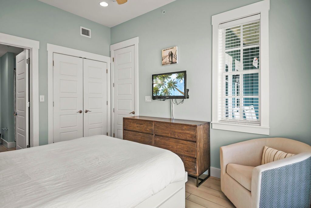 A bedroom with a large bed, a wooden dresser, a television, and a window with blinds.