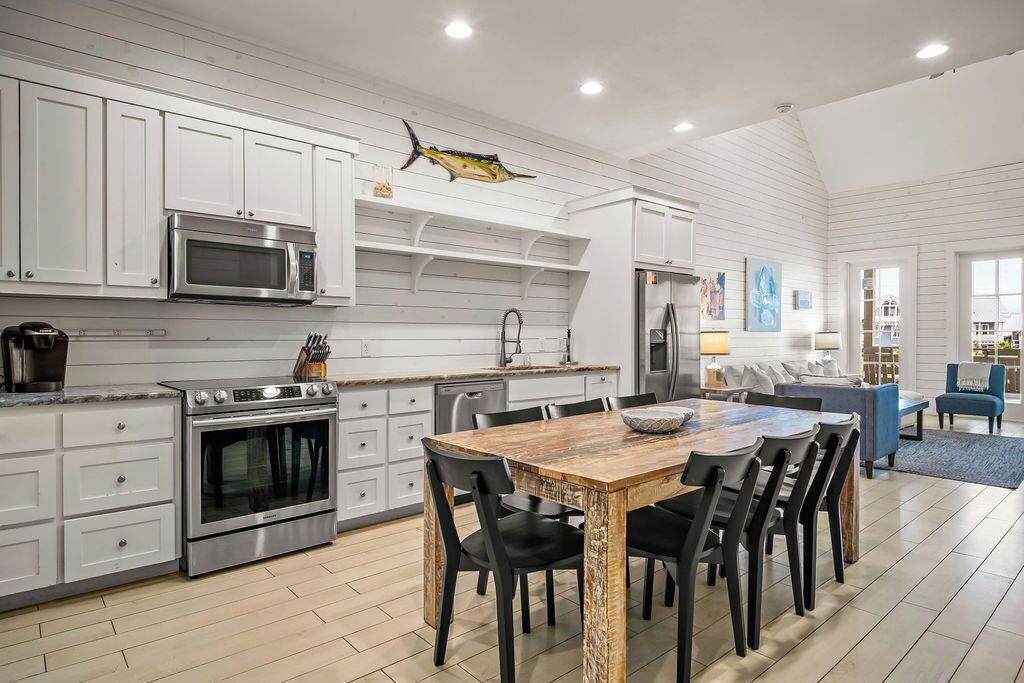 A modern kitchen with white cabinetry, stainless steel appliances, and a wooden dining table.