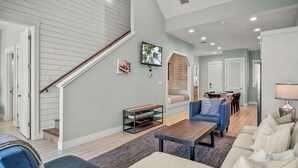 Un salon spacieux avec un escalier, un téléviseur et un coin repas.