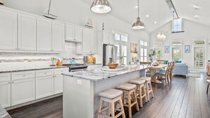 A spacious kitchen with white cabinets, a large island with stools, stainless steel appliances, and pendant lighting. - Casa al Mare 237 HI (Port Aransas)
