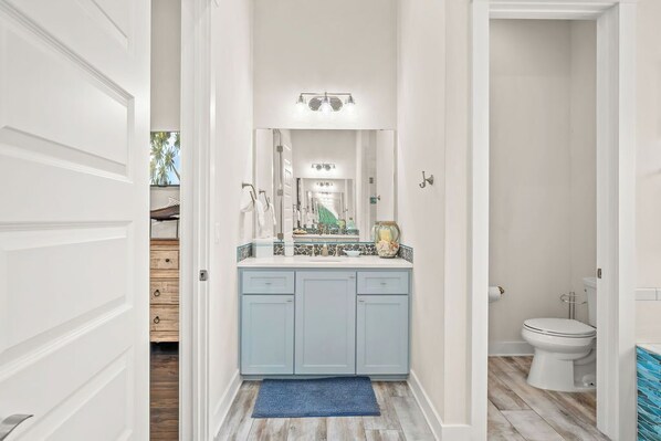 Bathroom features a central sink, mirror, and cabinets, with a toilet and shower area.