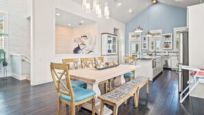 A modern kitchen with wooden dining table and chairs, pendant lights, and a decorative fish mural. - Casa al Mare 237 HI (Port Aransas)