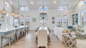 Una cocina amplia con una isla central, un comedor con candelabro y una sala de estar con sofá y mesa de centro.