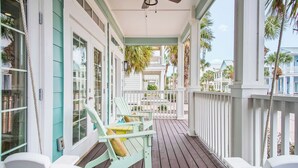 A wooden deck with white chairs and a table, overlooking a residential area with houses and palm trees. - Lovey Dovey 145 BE (Port Aransas)