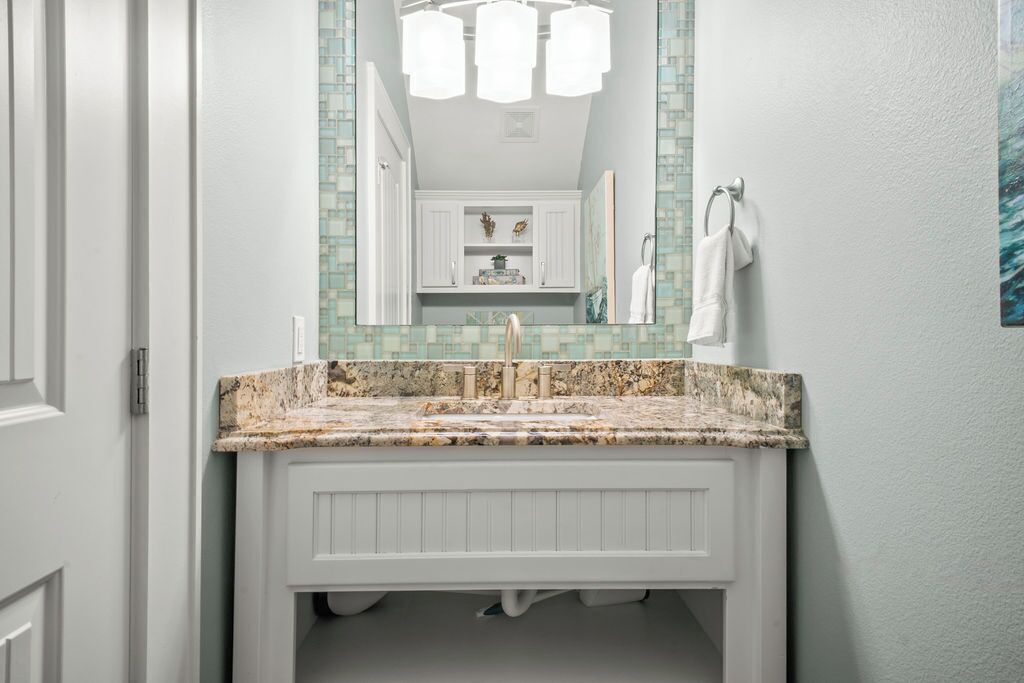A bathroom with a white vanity, a granite countertop, a mirror with a mosaic backsplash, and a towel rack.