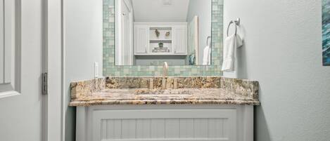 A bathroom with a white vanity, a granite countertop, a mirror with a mosaic backsplash, and a towel rack.