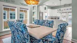 A dining area with a table and chairs, a chandelier, and a view of the kitchen and outside. - Lovey Dovey 145 BE (Port Aransas)