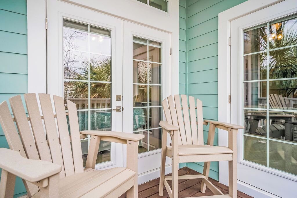 A porch with two wooden Adirondack chairs and a white door with glass panels.