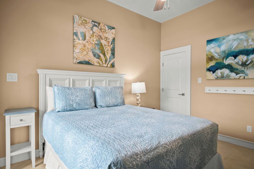 A bedroom with a large bed, a nightstand, a wall-mounted lamp, and two paintings.