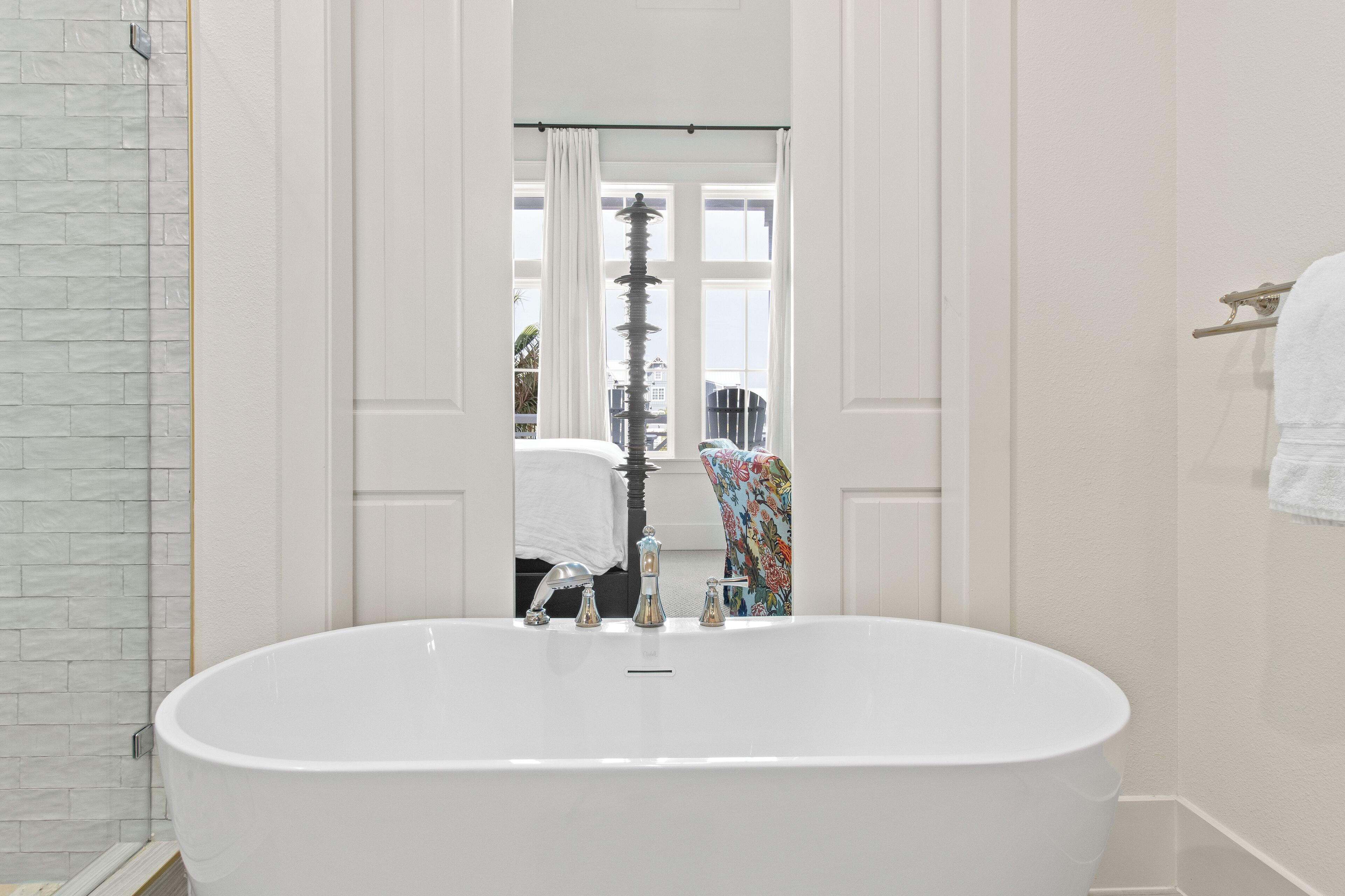 A bathroom with a large white bathtub, a mirror, and a window with curtains.