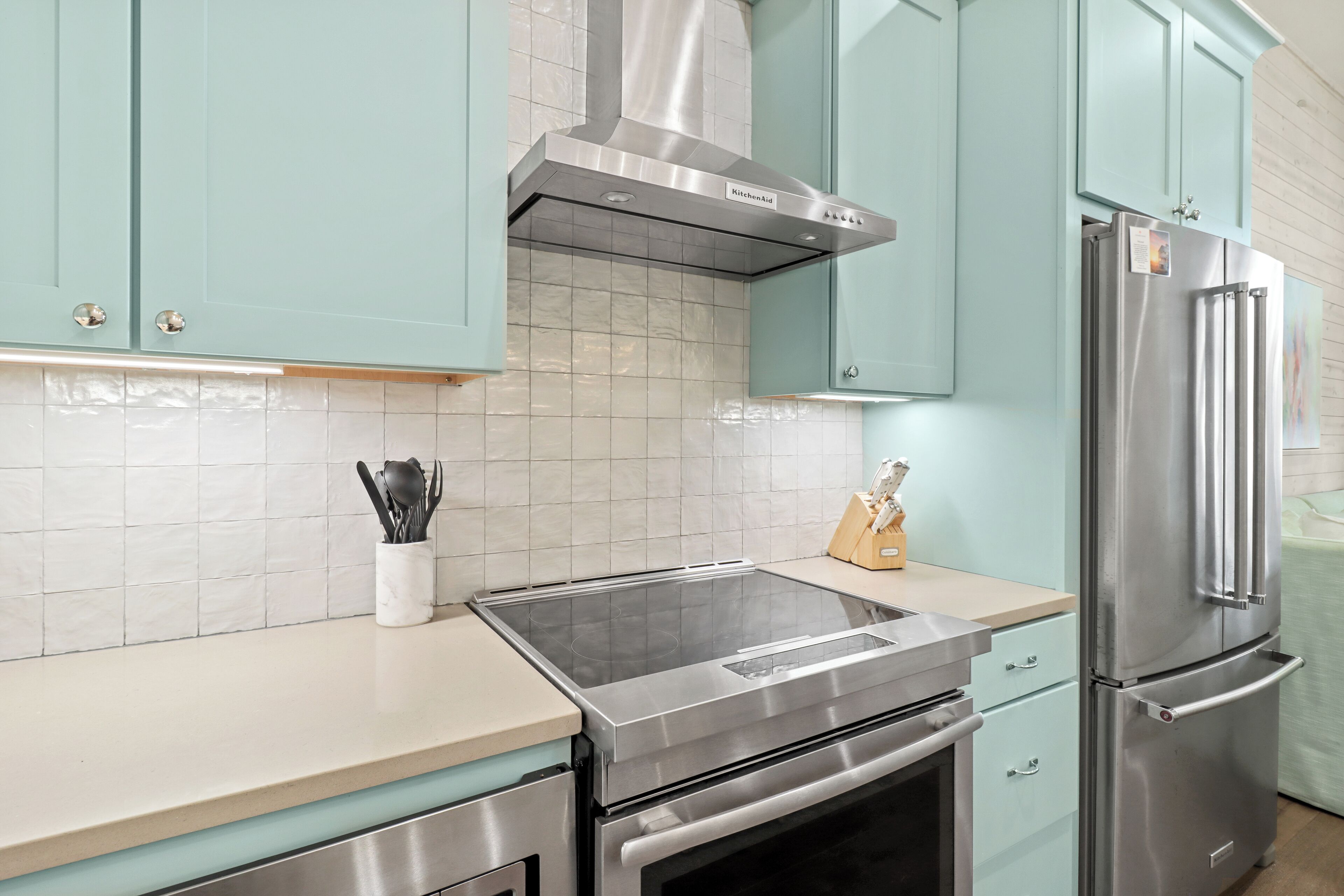 Una cucina con mobili color petrolio, una cappa aspirante in acciaio inossidabile e un frigorifero.