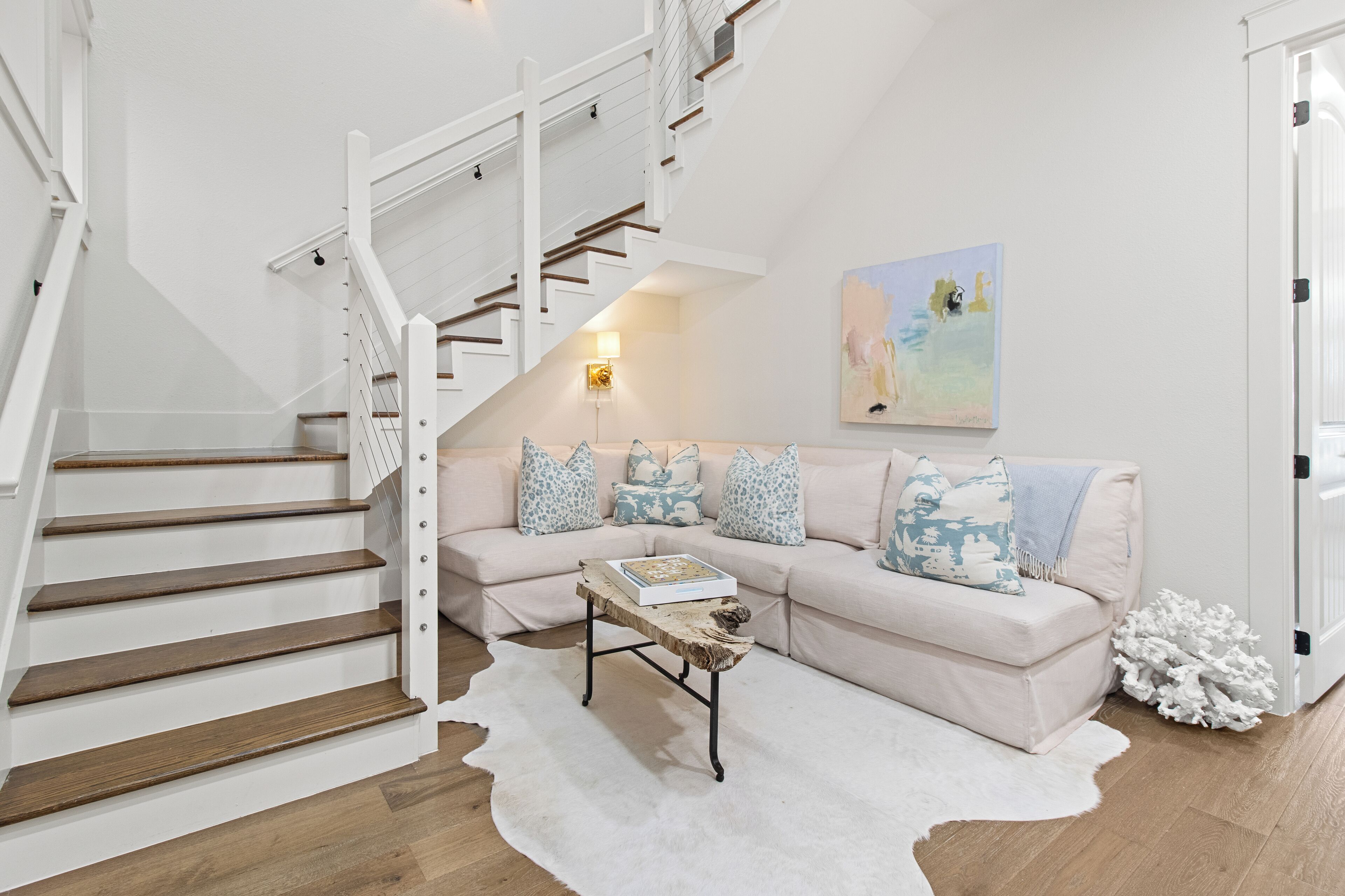 A staircase with wooden steps and white railings leading to a living area with a beige sofa, patterned cushions, and a white rug.