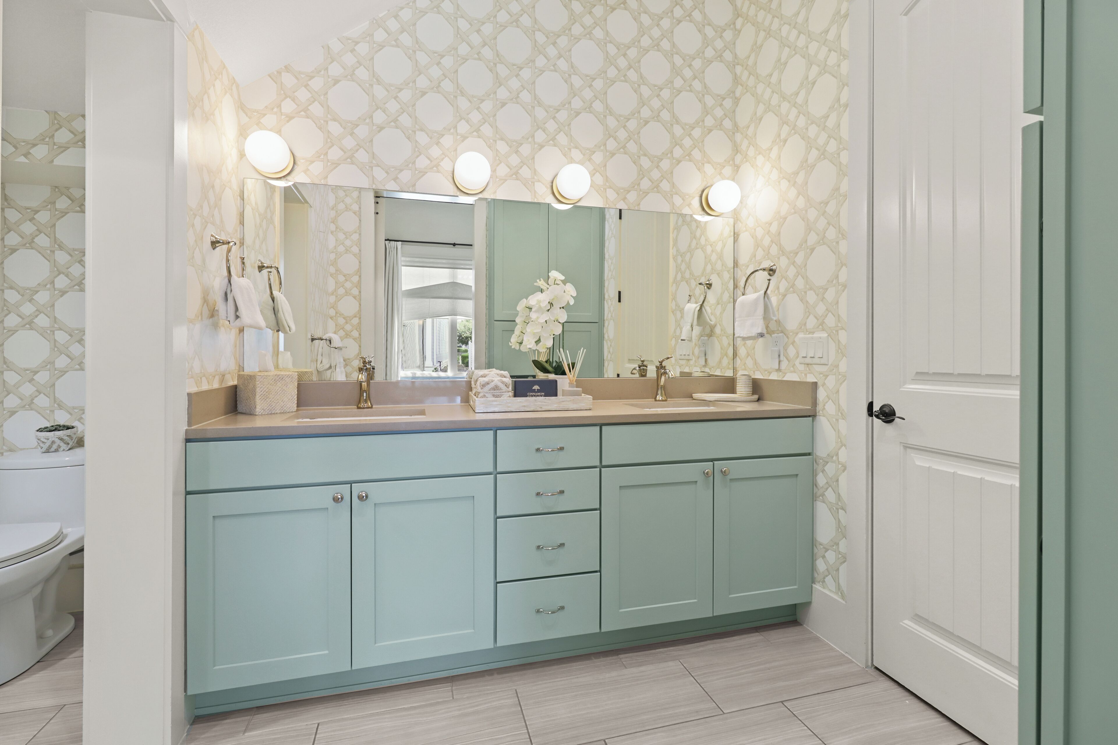 A bathroom with a light blue vanity, a large mirror with lights, and a toilet.