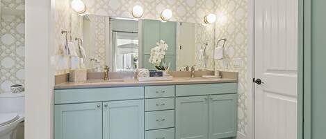 A bathroom with a light blue vanity, a large mirror with lights, and a toilet.