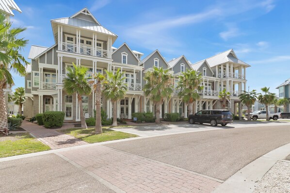 A multi-story residential building with a balcony, palm trees, and a paved driveway.