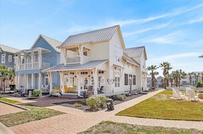 Una casa de estilo costero con un porche cubierto, varias terrazas y un jardín cuidado.