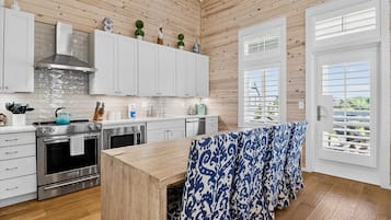A modern kitchen with wooden paneling, white cabinets, stainless steel appliances, and a view through the window.