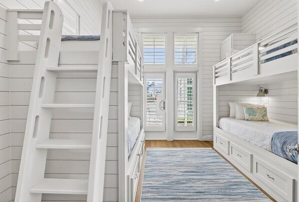 A room with bunk beds, a ladder, a door with glass panels, and a blue striped rug.