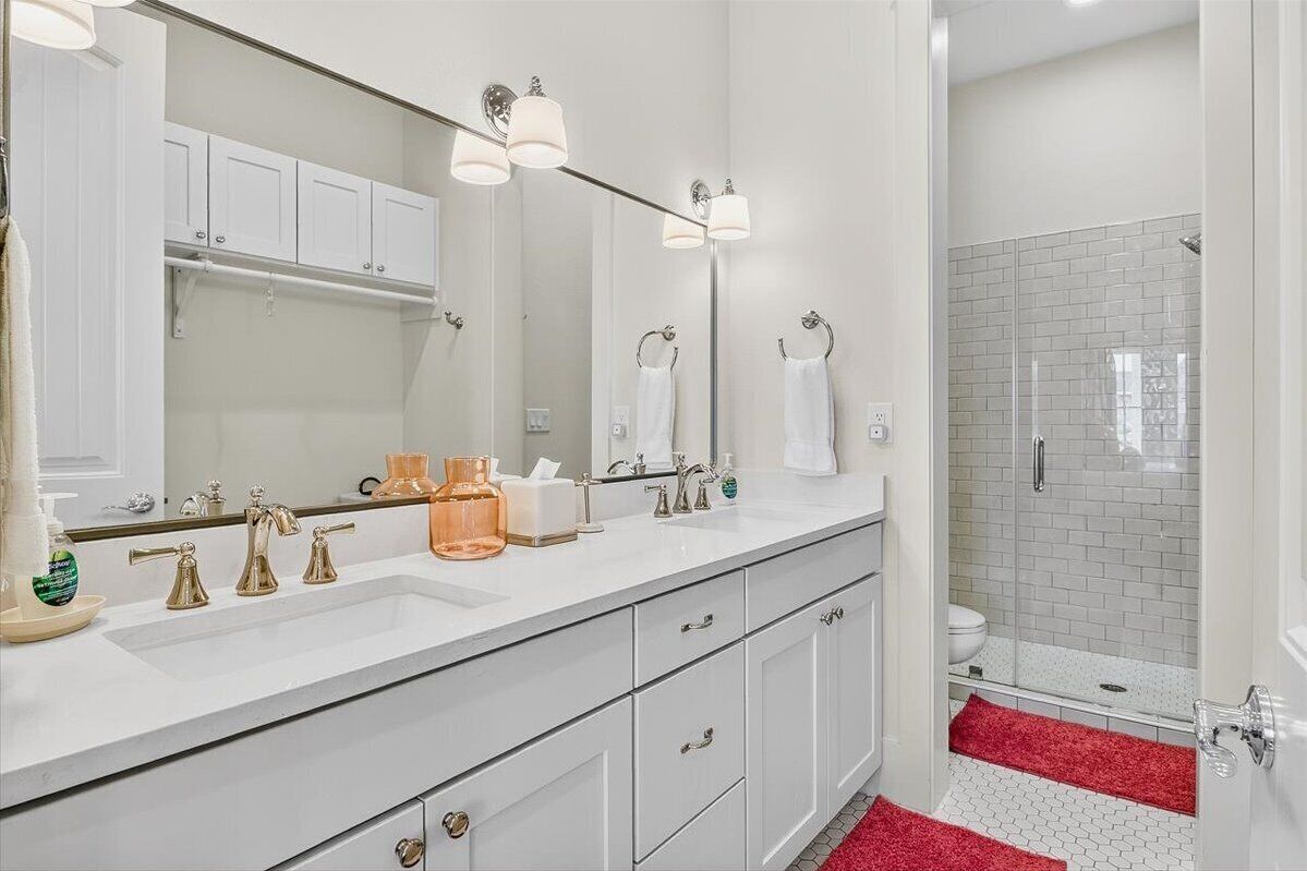 A modern bathroom with a white vanity, gold faucets, and a glass shower enclosure.