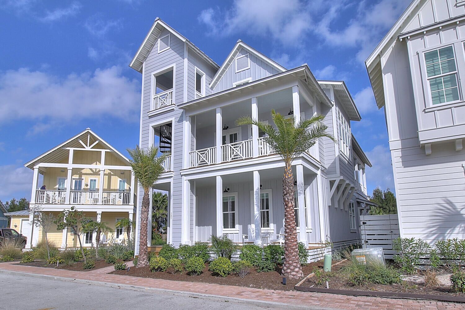 Una casa a due piani con un balcone e un portico, circondata da un giardino con palme.
