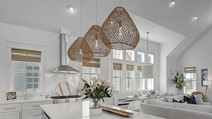 A modern kitchen with white cabinetry, a large island, and hanging woven light fixtures. - Seas the Day 131 WI (Port Aransas)