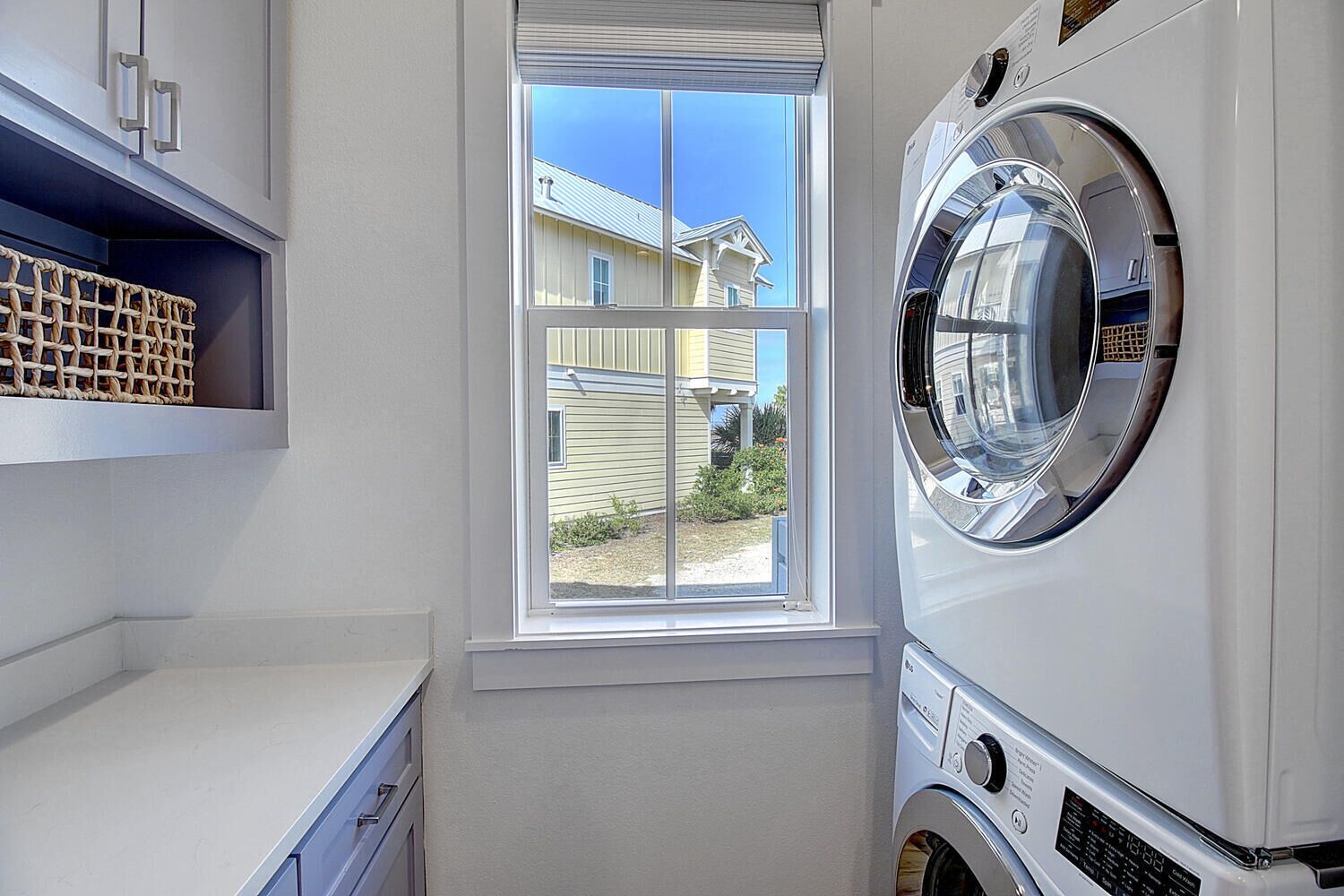 A laundry room with a large washing machine, a window with a view of a house, and a shelf with baskets.