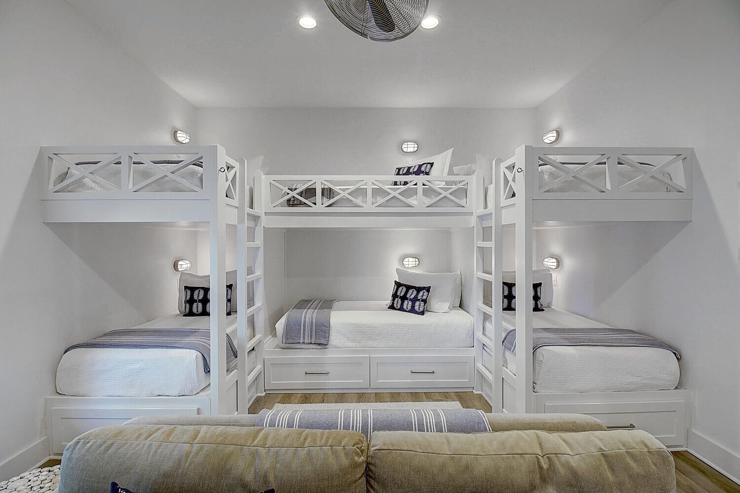 A bunk bed room with a central bed, two smaller beds on either side, and a sofa at the bottom.