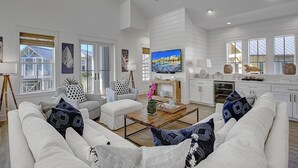 A spacious living room with a large TV, white furniture, and a view of the outside. - Seas the Day 131 WI (Port Aransas)