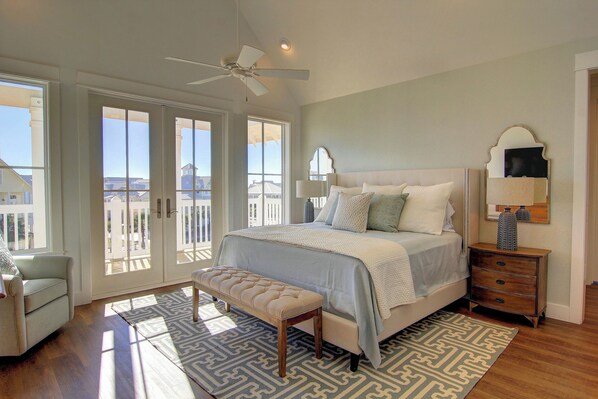 A bedroom with a large bed, a bench, a dresser, and a ceiling fan.