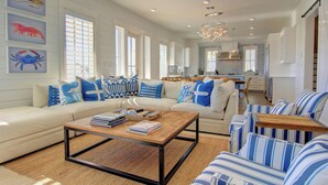 A spacious living room with a large sofa, a coffee table, striped chairs, and artwork on the walls. - Salt and Light 192 RO (Port Aransas)