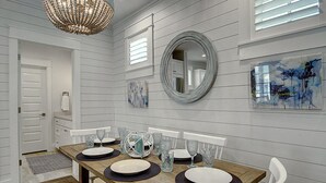 A dining area with a wooden table set for four, a large mirror, and abstract art on the walls. - Seahorse Cottage 230 RO C1 (Port Aransas)