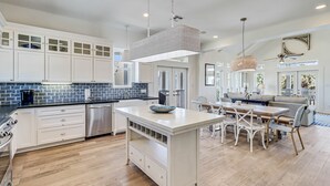 A modern kitchen with white cabinetry, a central island, and a dining area with a table and chairs.