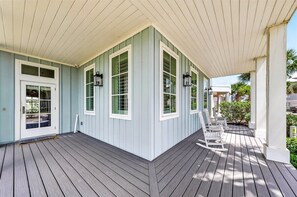 A covered porch with a wooden deck, a white door, and two windows with white frames.