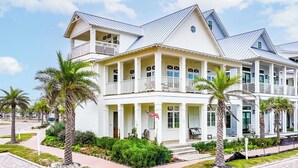 A two-story white building with balconies, a flag, and palm trees. - Summer Catch 401 COA (Port Aransas)