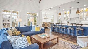 A spacious living room with a blue sofa, wooden coffee table, and a kitchen area with bar stools and pendant lighting. - Summer Catch 401 COA (Port Aransas)
