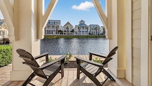 A wooden deck with two Adirondack chairs overlooking a body of water and a row of houses. - Sun Chaser Cottage 205 Fiv-d (Port Aransas)