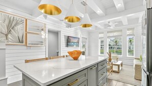 A modern kitchen with a large island, pendant lighting, and a view to the outdoors. - Sun Chaser Cottage 205 Fiv-d (Port Aransas)