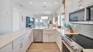 A modern kitchen with stainless steel appliances, white cabinetry, and a central island with seating. - Seaside Cabana TC 10302 (Port Aransas)