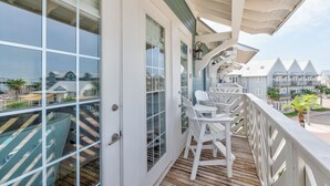 A balcony with white chairs, a wooden deck, and a view of other buildings. - Seaside Cabana TC 10302 (Port Aransas)