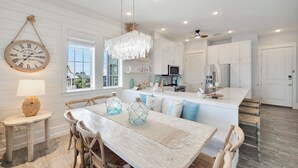 A spacious kitchen with white cabinetry, a central island, and a dining area with a wooden table and chairs. - Seaside Cabana TC 10302 (Port Aransas)