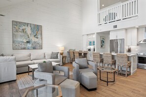 A spacious living area with a high ceiling, a dining area with wicker chairs, and a kitchen with modern appliances. - Sandy Bottoms Beach House TC 5104 (Port Aransas)