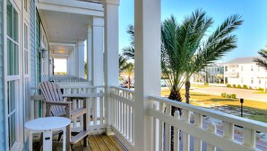 A wooden deck with a white railing, a table, and two Adirondack chairs.