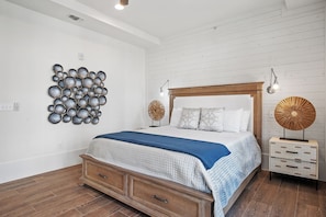 A bedroom with a wooden bed, a wall-mounted decorative piece, bedside lamps, and a nightstand. - Sandy Bottoms Beach House TC 5104 (Port Aransas)