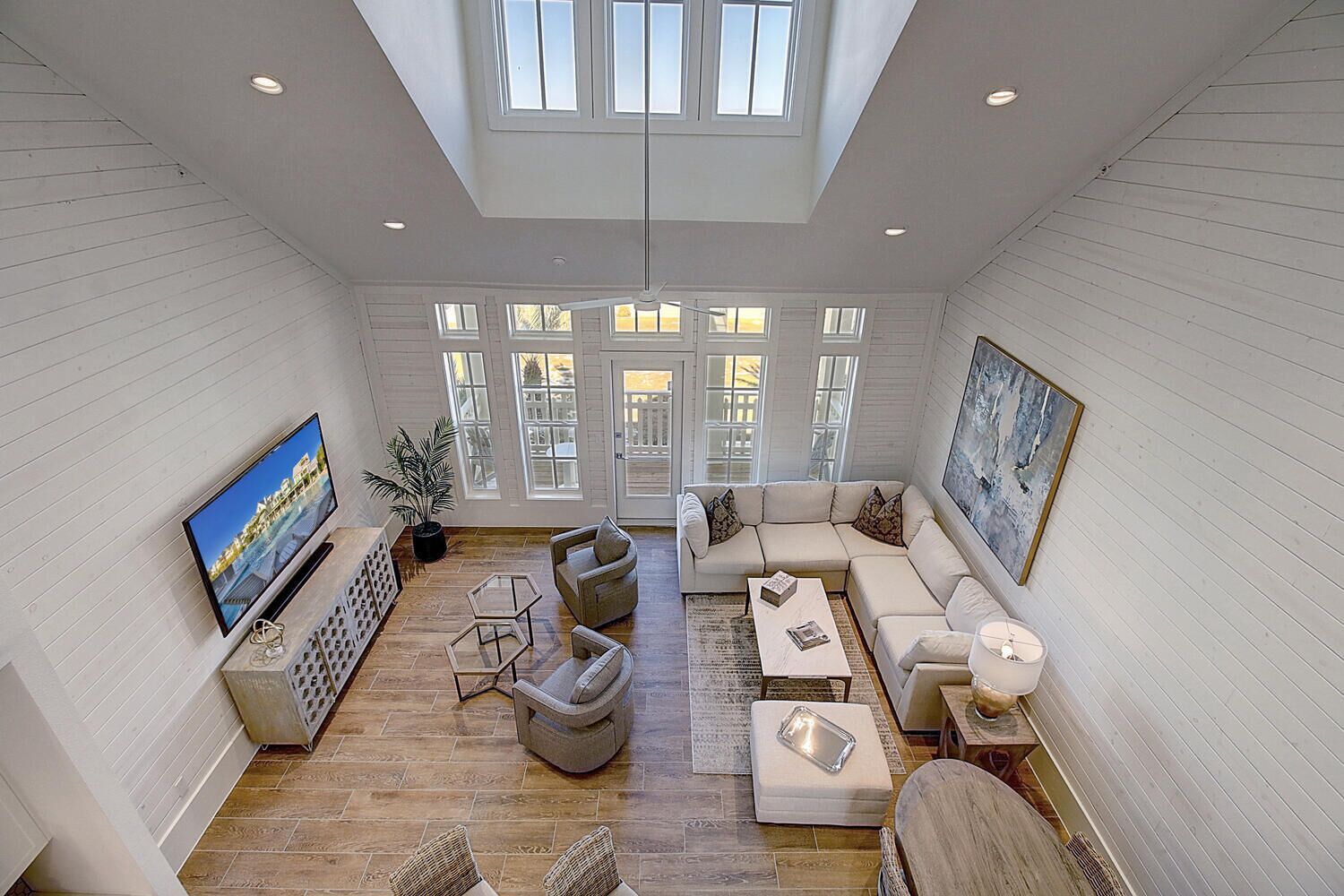 A spacious living room with a large TV, comfortable seating, and a view of the outdoors through large windows.