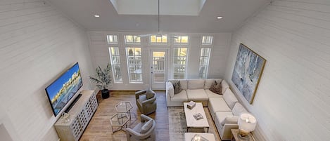 A spacious living room with a large TV, comfortable seating, and a view of the outdoors through large windows.