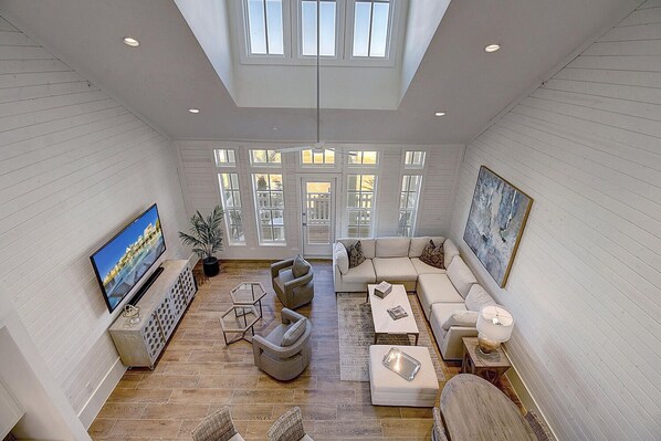 A spacious living room with a large TV, comfortable seating, and a view of the outdoors through large windows.