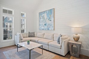 A living room with a beige sectional sofa, a marble coffee table, a side table with a lamp, and a large abstract painting on the wall.