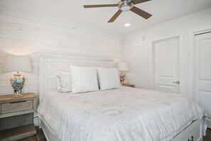 A bedroom with a bed, a nightstand, a lamp, a ceiling fan, and a door.