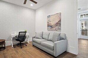 Ein moderner Arbeitsraum mit einem grauen Sofa, einem schwarzen Bürostuhl und einem weißen Schreibtisch.