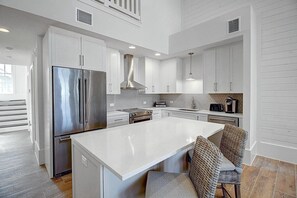 Una cocina moderna con armarios blancos, un refrigerador de acero inoxidable, una isla central y una zona de comedor con sillas de mimbre.